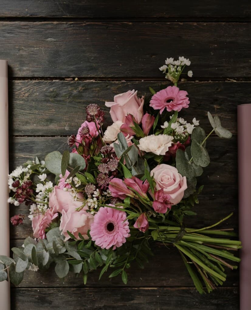 A hand-tied bouquet of pink roses, gerberas and eucalyptus on dark wood