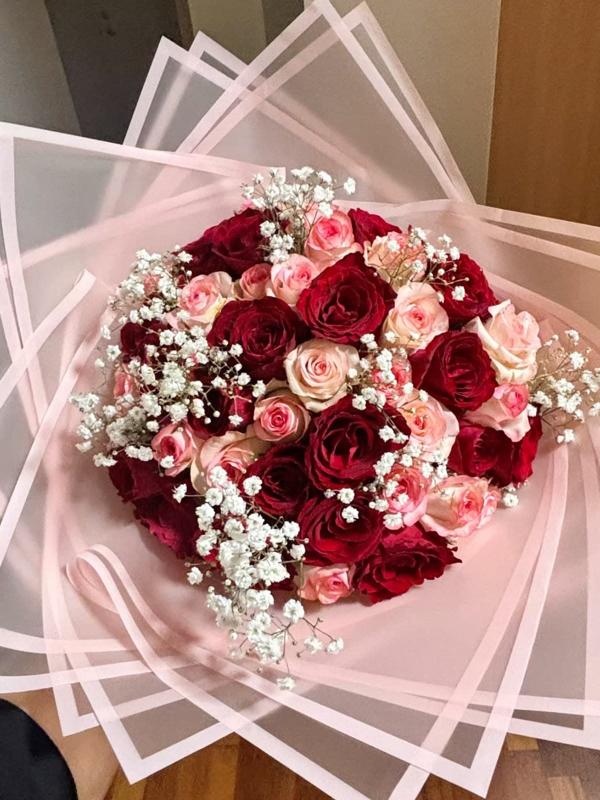 Deep red and blush pink roses with baby's breath, wrapped in sheer pink